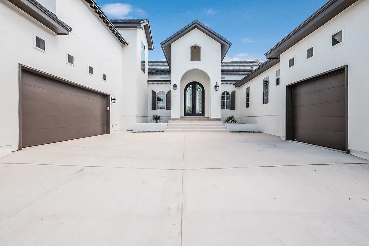 Modern house plan exterior with a two-car garage, arched entry with double doors, and a stucco facade.