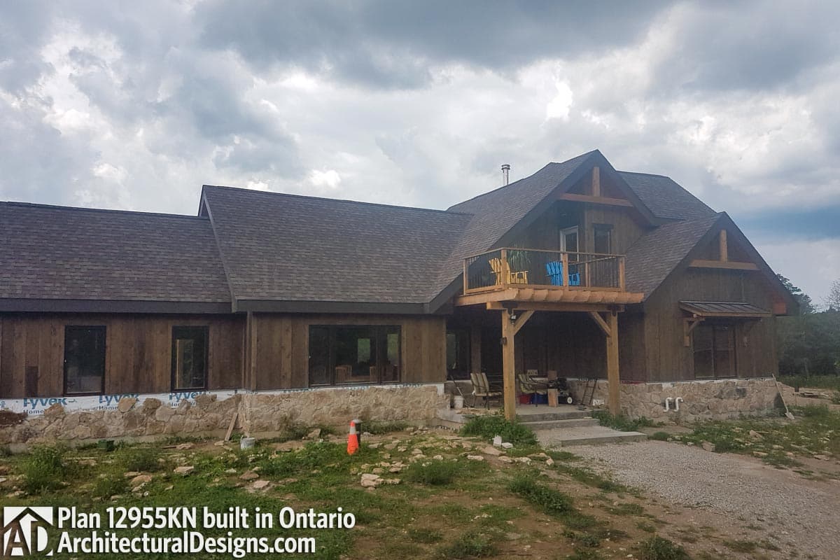 House plan exterior featuring a timber frame, stone foundation, upper deck, and multiple gables.