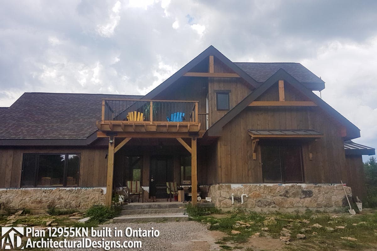 House plan exterior featuring wood siding, stone foundation, upper balcony, and exposed timber framing.