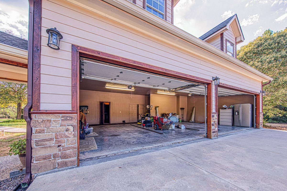 House plan exterior view of a three-car garage with stone accents, two open garage doors, and a dormer above.