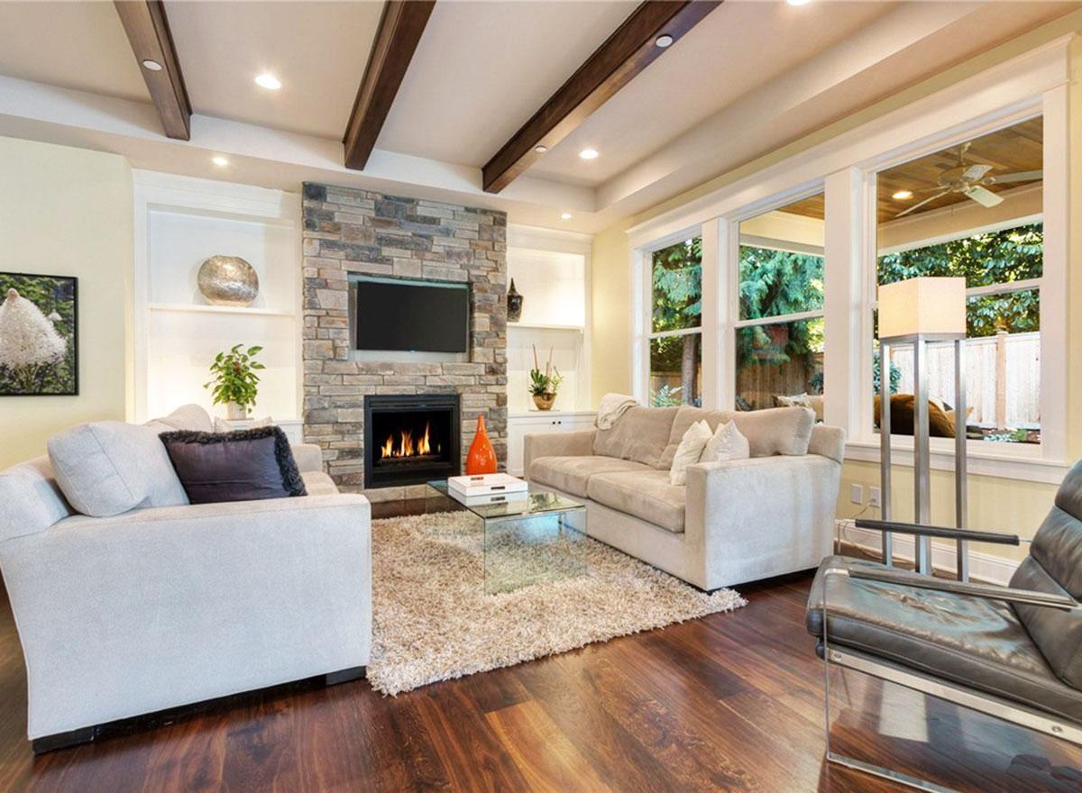 Living room with stone fireplace, gas fire, TV, beamed ceiling, large windows, and hardwood floors.
