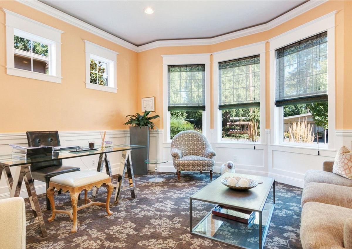 Office with glass desk, patterned chair, and bay windows overlooking a backyard.