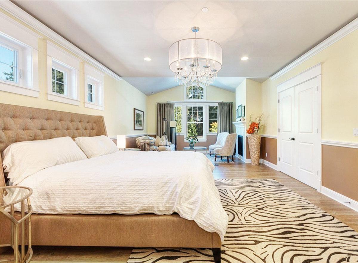 Primary suite featuring tufted bed, fireplace, seating area, and large windows with vaulted ceiling.