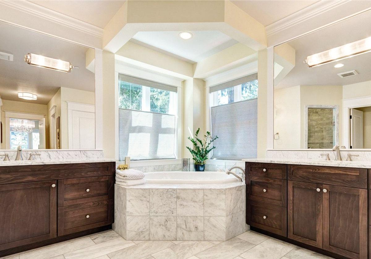 Master bathroom with corner soaking tub, dual vanities with dark wood cabinets, marble countertops, and large mirrors.