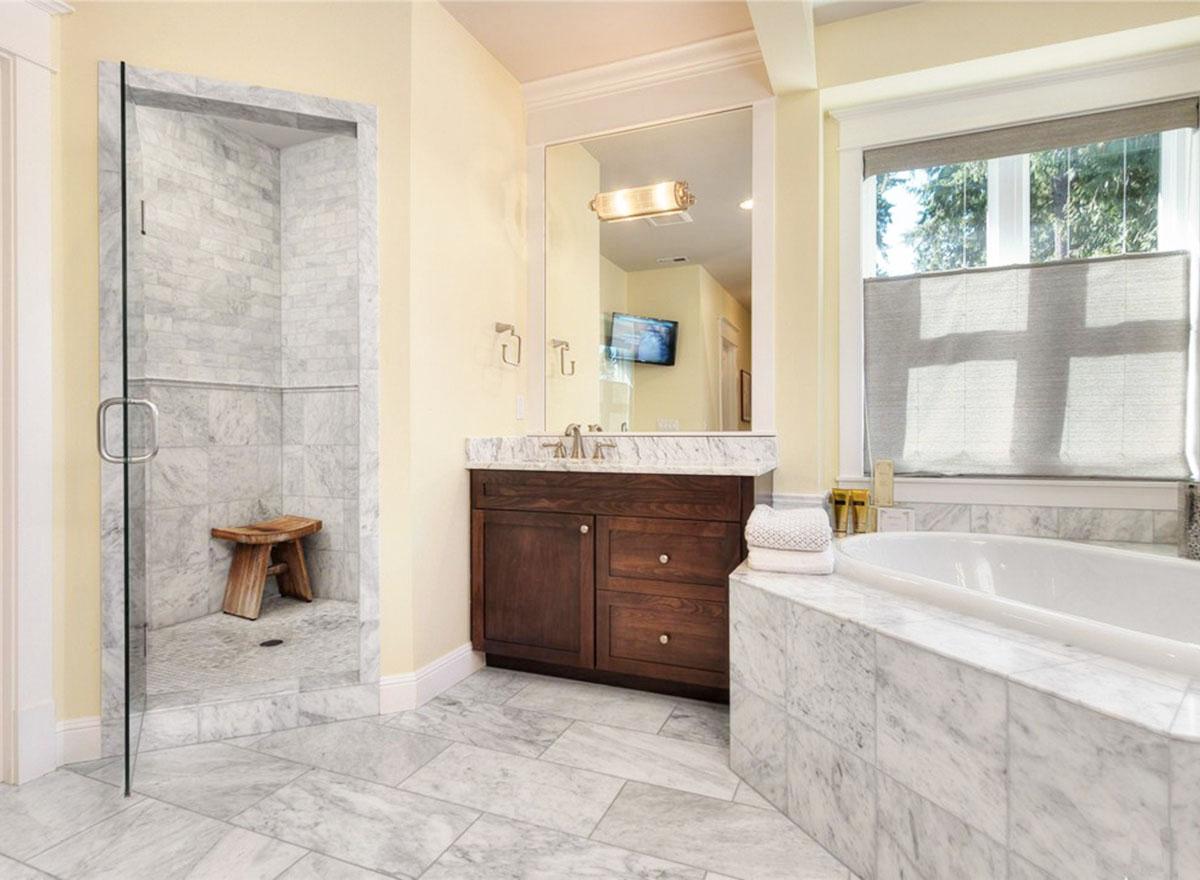 Bathroom with marble tile shower, dark wood vanity with granite countertop, and bathtub.
