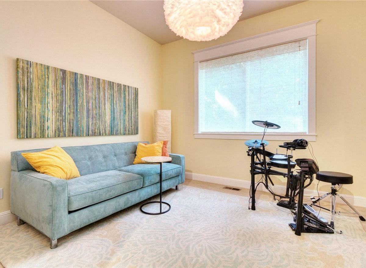 Living room with blue sofa, abstract wall art, digital drum set, and large window with blinds.
