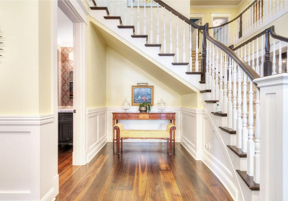Interior view of a staircase with white balusters and dark treads, a console table with bench, and hardwood flooring.