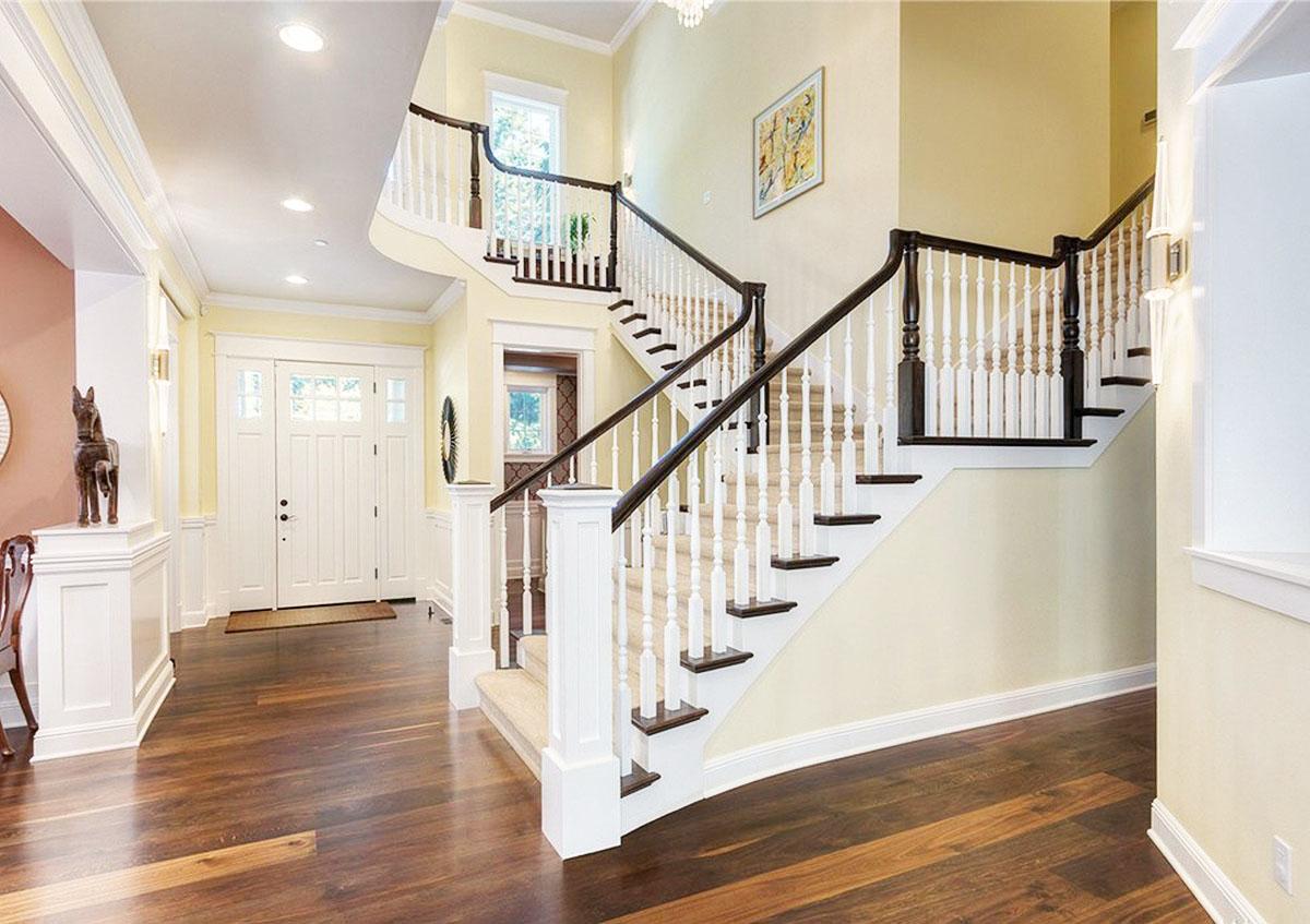 Interior view of a grand foyer with a curved staircase, white paneled wainscoting, and double entry doors.