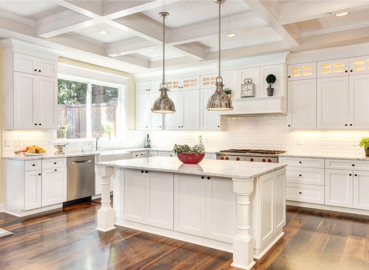 Kitchen with white cabinetry, coffered ceiling, large island with marble countertop, and stainless steel appliances.