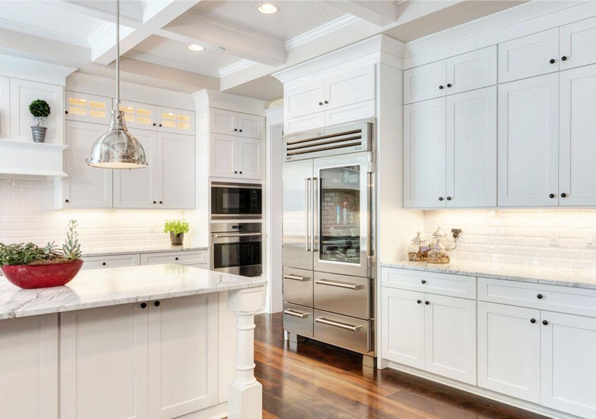 Kitchen interior with white cabinetry, marble countertops, stainless steel Sub-Zero refrigerator, and coffered ceiling.