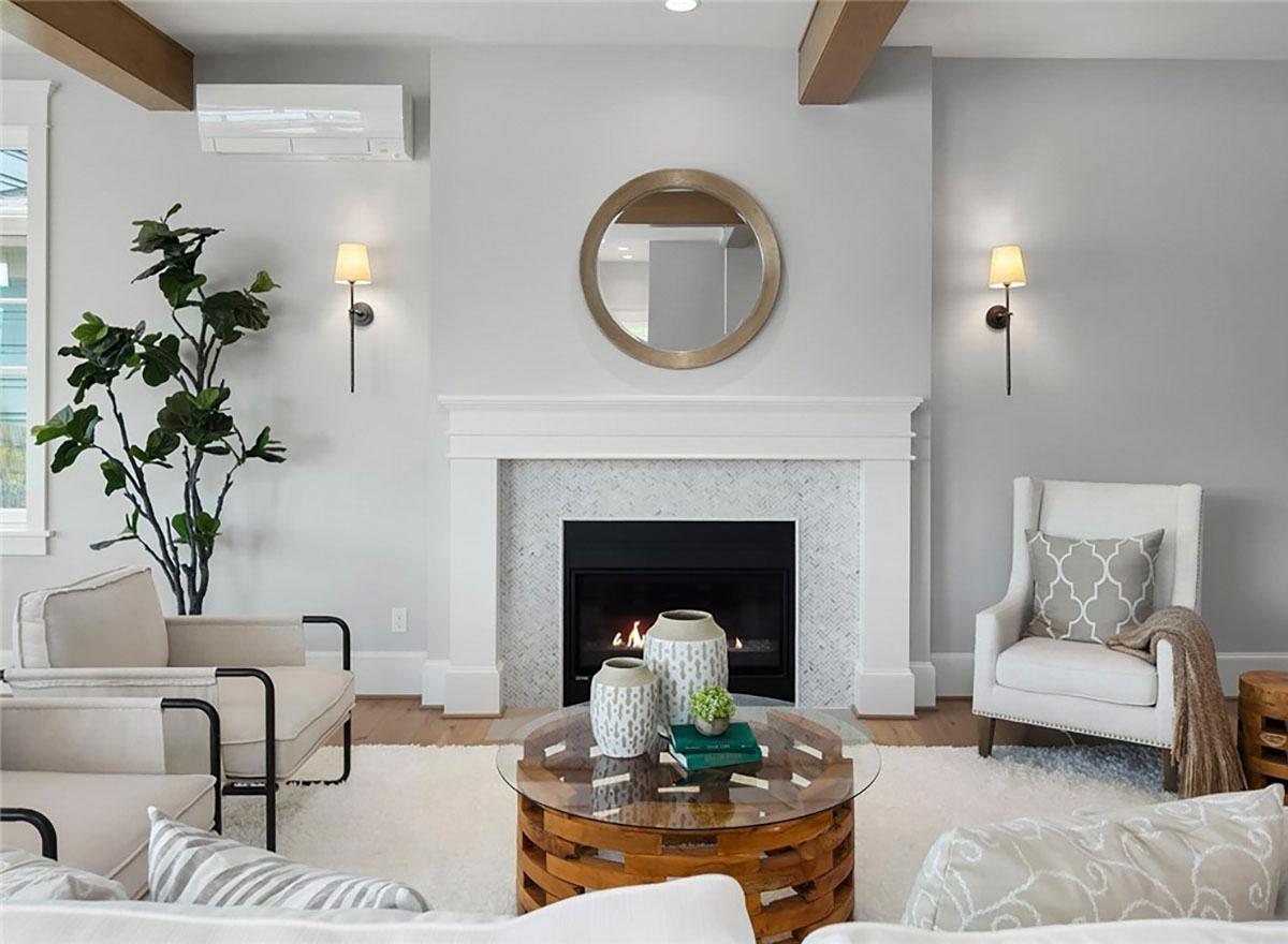 Living room featuring a fireplace with herringbone tile surround, mantel, and a circular mirror above. Exposed beams are visible on the ceiling.
