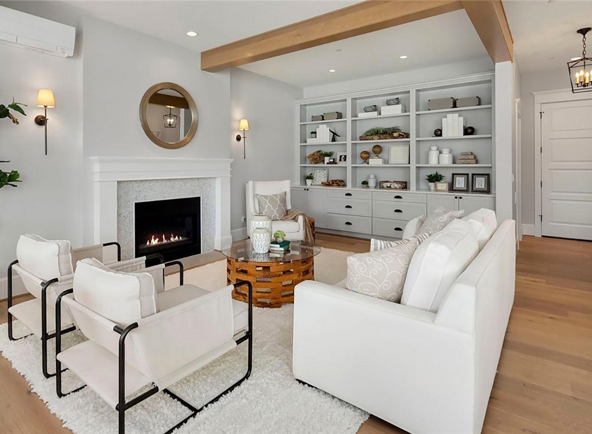 Living room with fireplace, built-in bookshelves, exposed wooden beams, and light-colored seating.