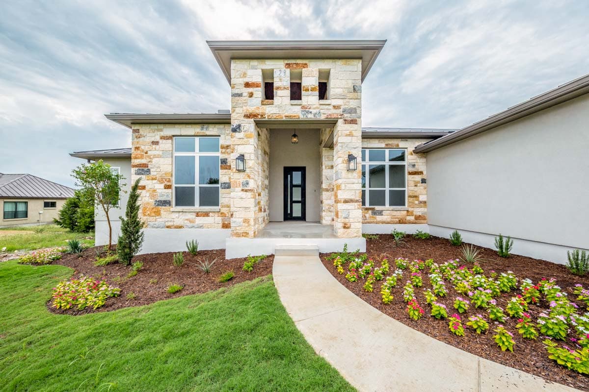 House plan exterior with stone facade, modern roofline, and prominent entryway tower with geometric windows.