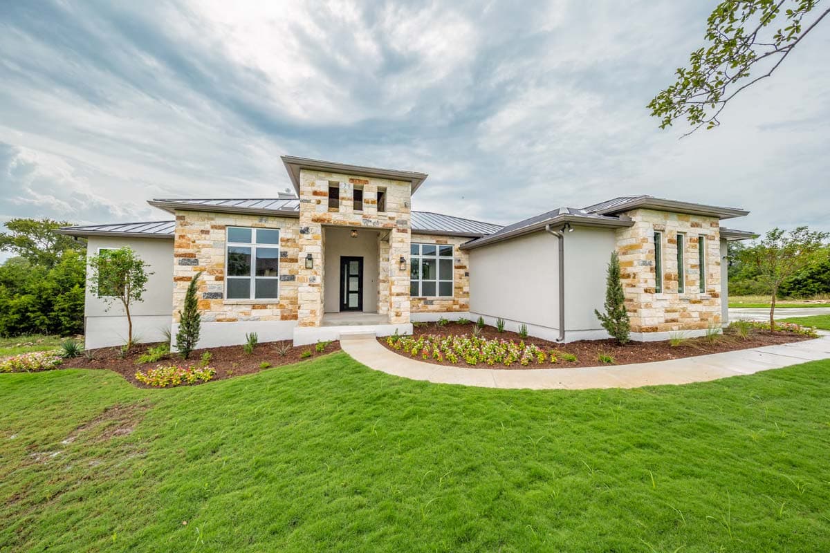 House plan exterior with stone and stucco facade, flat roof, and a covered entry. Features large windows and a manicured lawn.