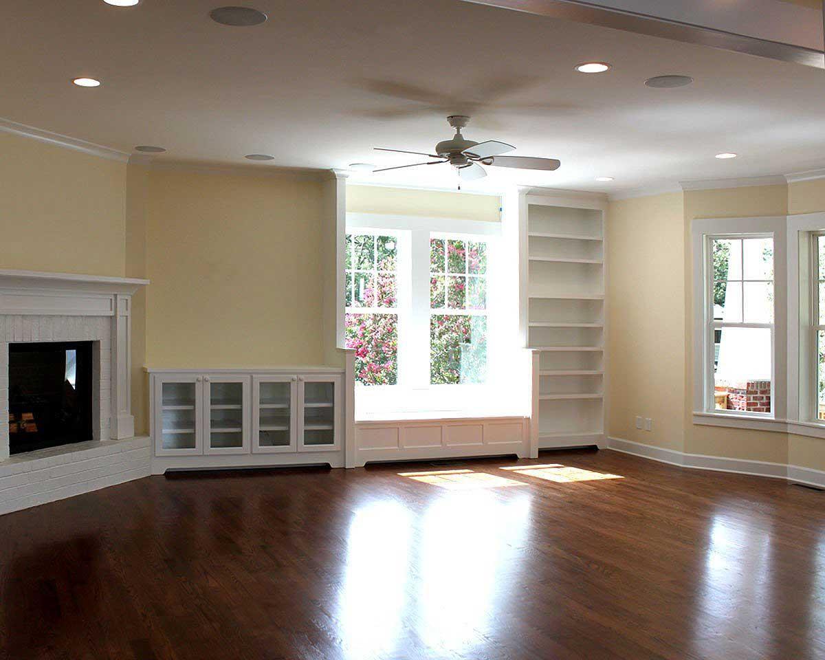 Interior view of living room with fireplace, built-in bookcases, window seat, and large windows.