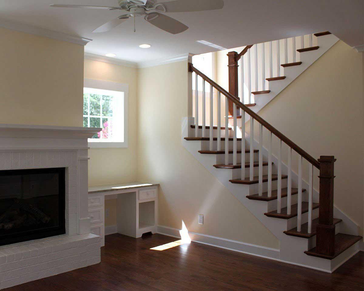 Interior view of a living area with a white brick fireplace, built-in desk, and wood staircase with white balusters.
