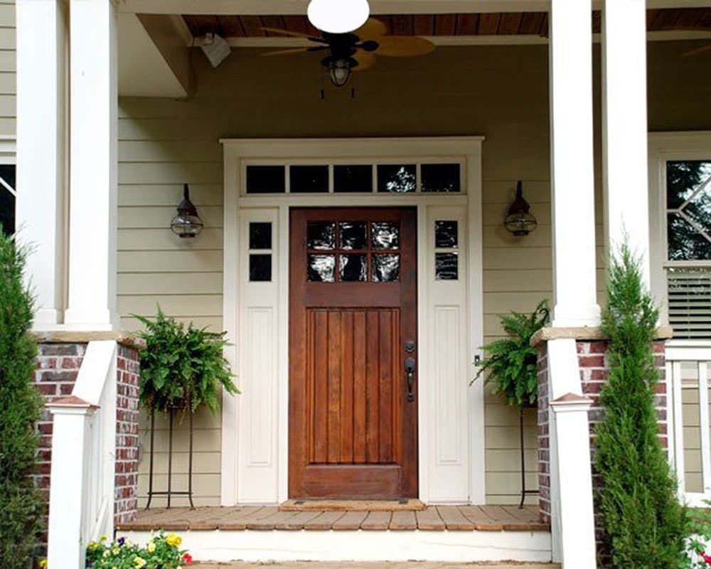 Craftsman style house plan exterior with wooden door, glass transom, sidelights, porch with white columns, brick base, and fan.