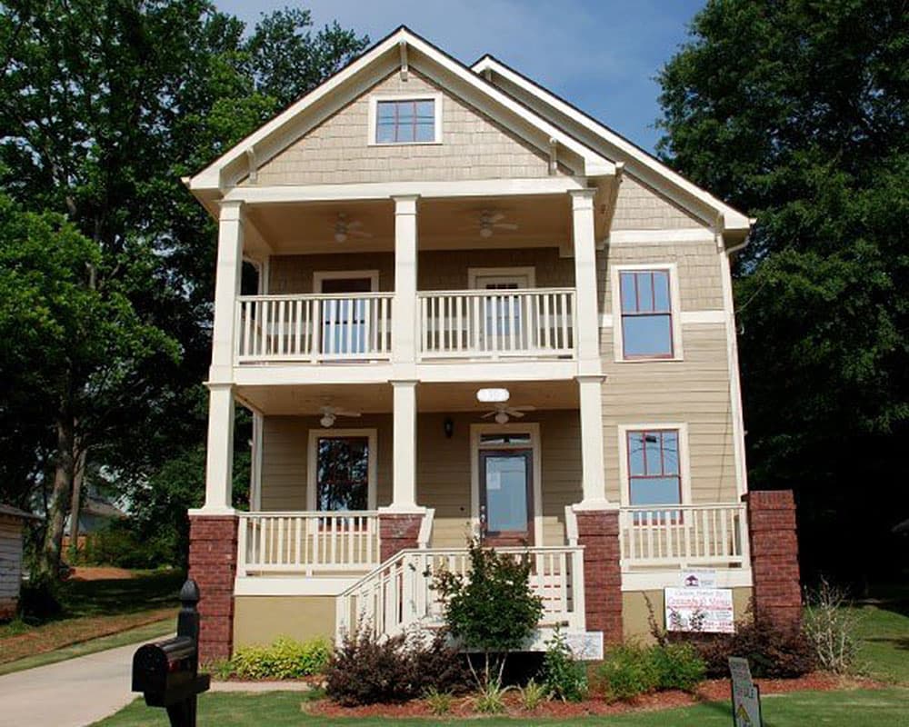 House plan exterior: two-story home with dual covered balconies, gable roof, shingle siding, and brick accents.