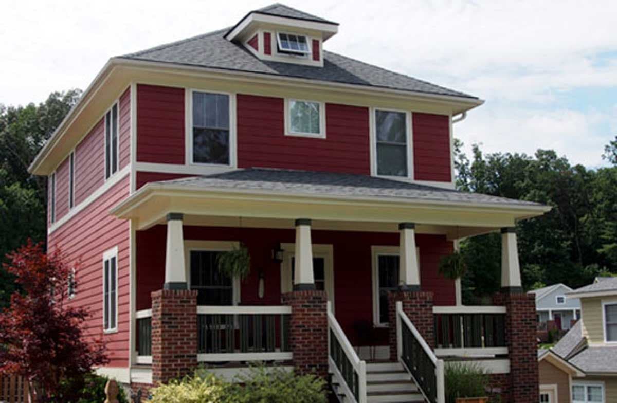 Two-story house plan exterior with red siding, gabled dormer, and wraparound porch with brick piers.