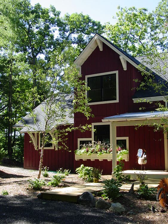 Modern farmhouse house plan exterior with deep red siding, exposed rafter tails, and a covered porch with white columns.
