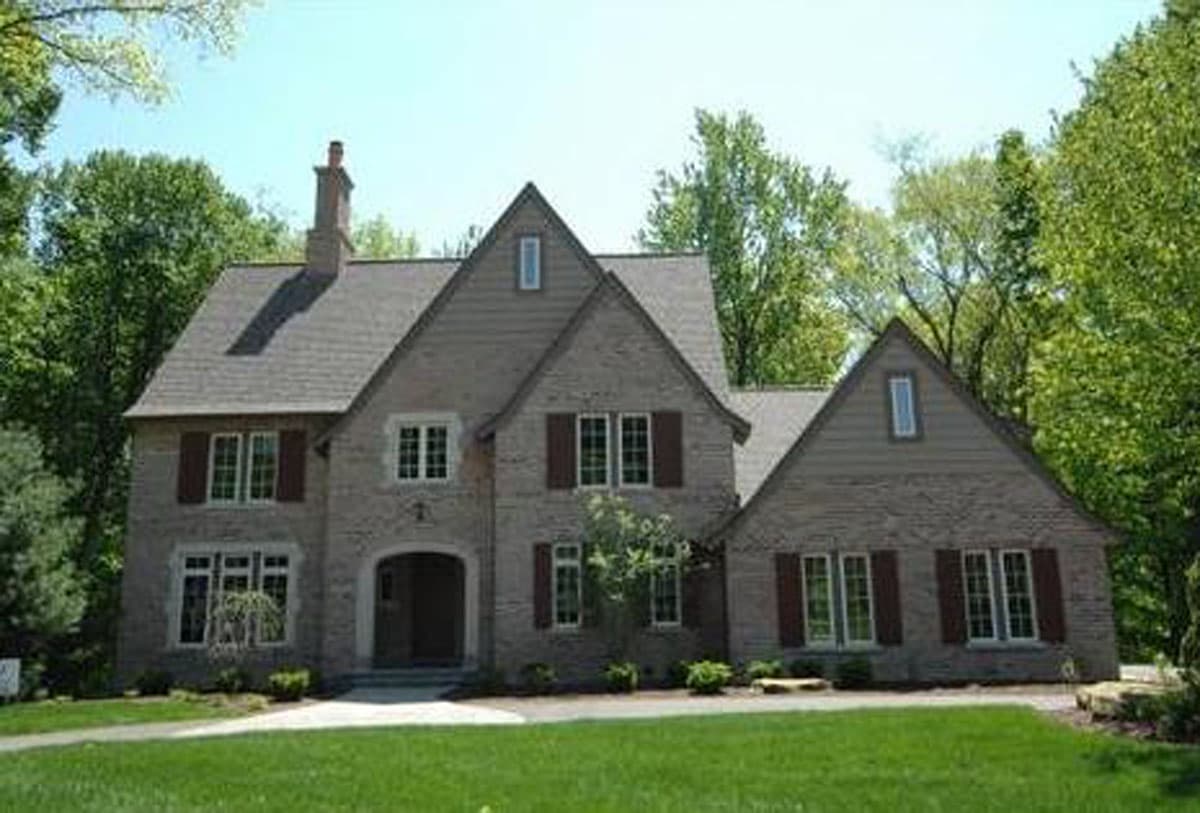 Two-story brick house plan with a prominent gable, arched entryway, dormer windows, and multiple window groupings with shutters.
