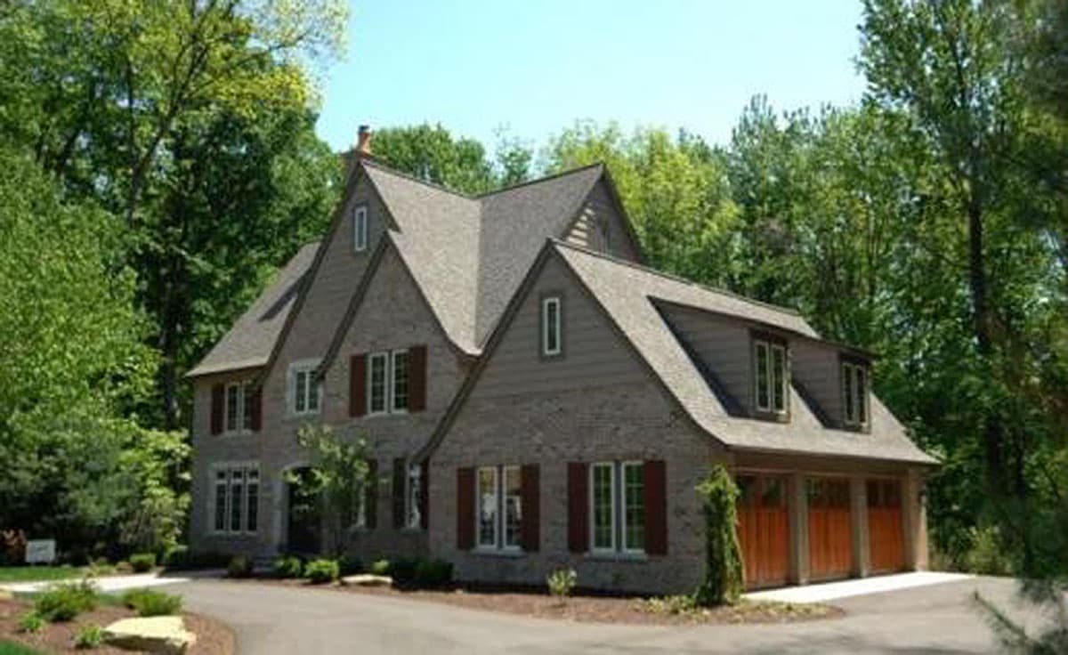 House plan exterior of a two-story home with brick facade, gables, dormer windows, and a three-car garage.
