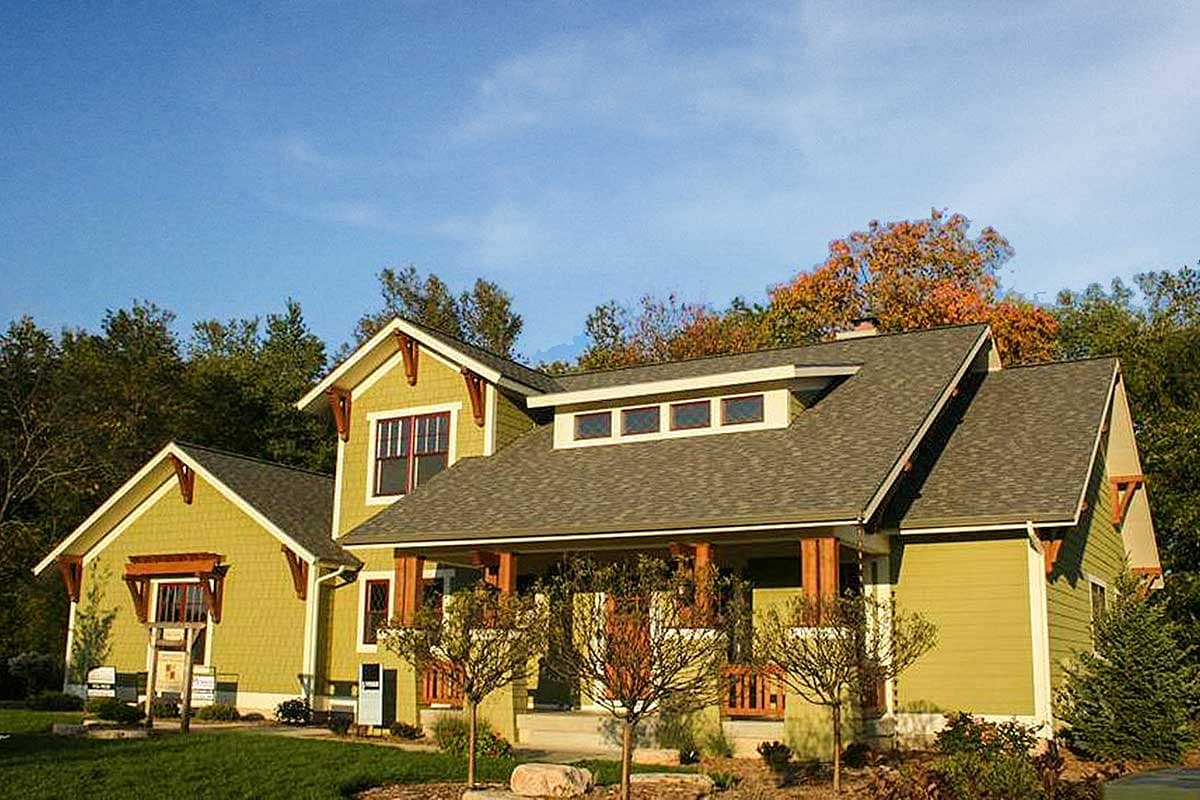 House plan exterior: Craftsman style, two stories, prominent gables with exposed rafter tails, wide porch with timber supports.