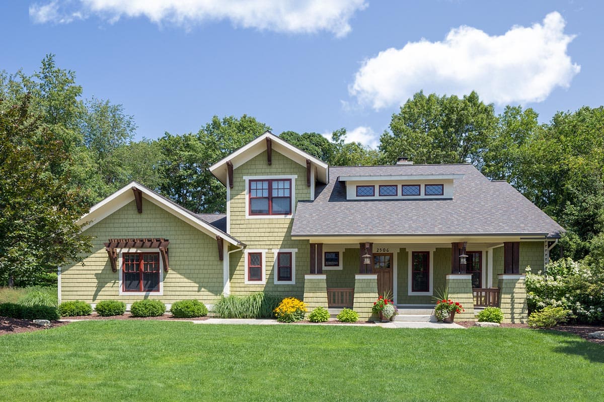 Craftsman house plan exterior with two stories, gabled roof, and a covered front porch with exposed rafters. Includes dormers and decorative trim.