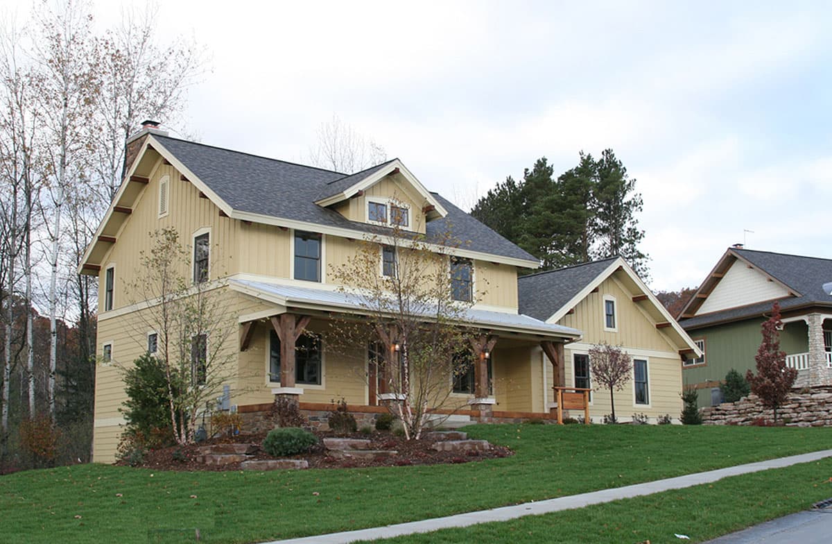 House plan exterior. Two-story Craftsman home with a gabled roof, prominent front porch with wood columns, and multiple dormers.
