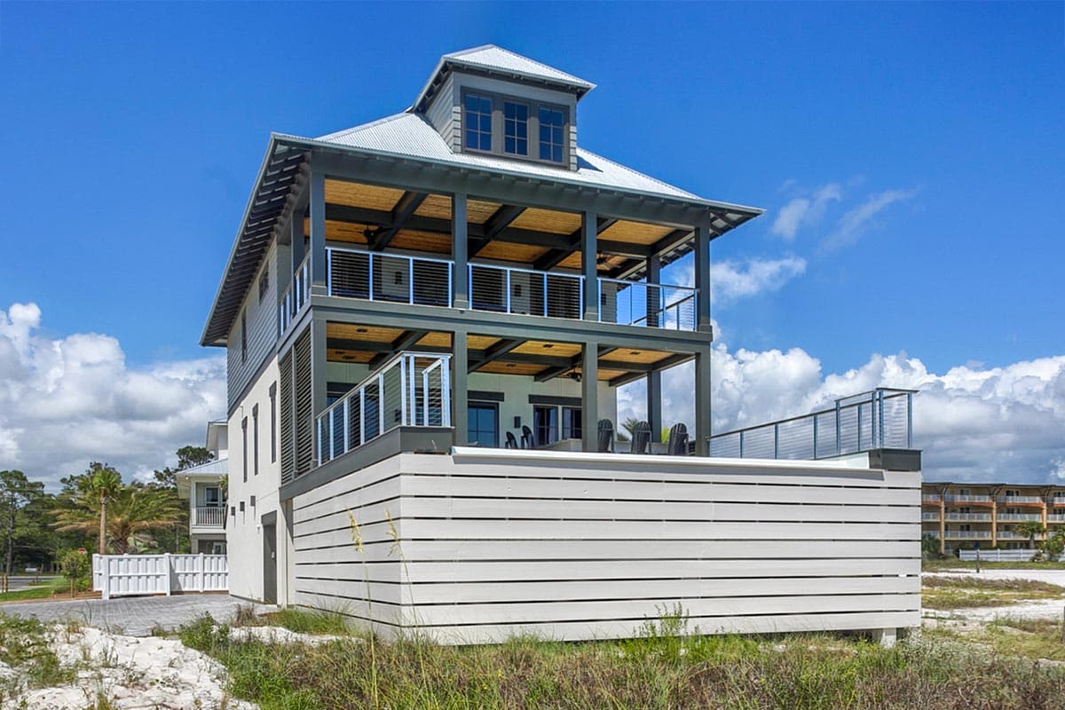 House plan exterior. Multi-story design with covered balconies. Features include a metal roof, open-air porch, and a dormer on the upper level.