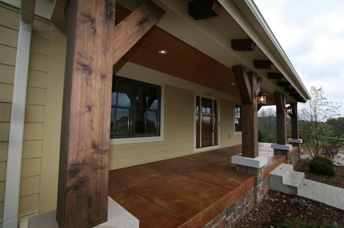 House plan exterior with exposed timber framing, covered porch, stone foundation, and multiple windows.