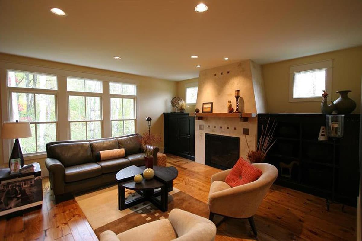Living room with leather sofa, fireplace, large windows, and wooden floors. Interior rendering.