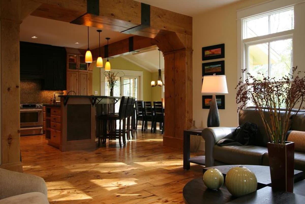 Open-concept living space with exposed wood beams, a kitchen island with bar stools, and a dining area beyond.