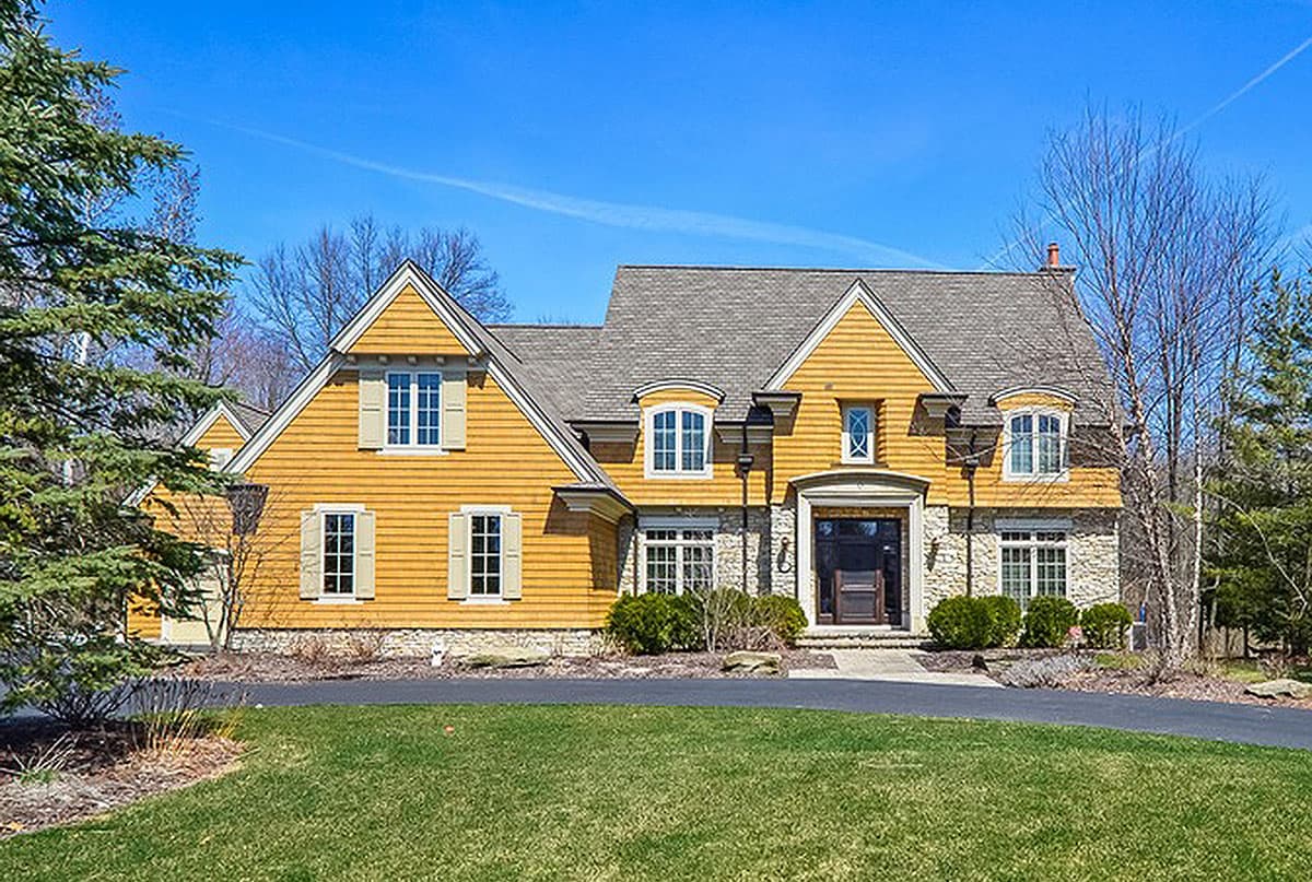 House plan exterior, two stories, stone foundation, yellow siding, multiple gables, dormer windows, and covered entry.