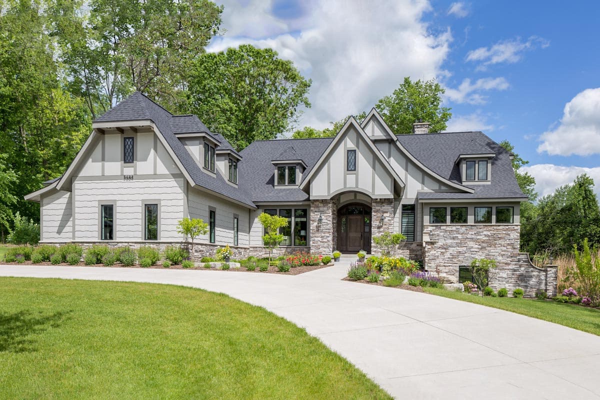 House plan exterior in Tudor style with stone facade and multiple gables. Features a steeply pitched roof, dormers, and an arched entry.
