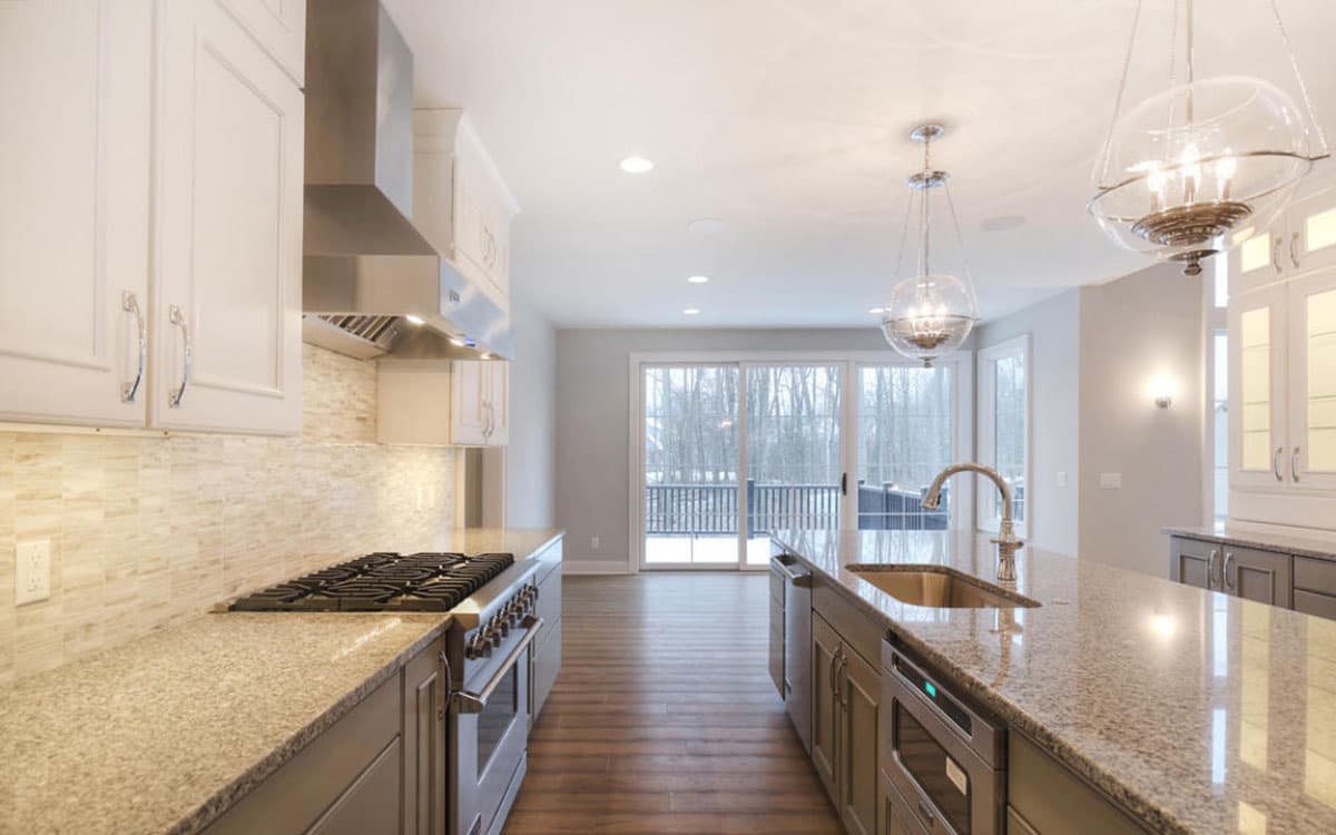 Kitchen with white cabinets, stainless steel range, granite countertops, and island with sink. Sliding glass doors open to a deck.