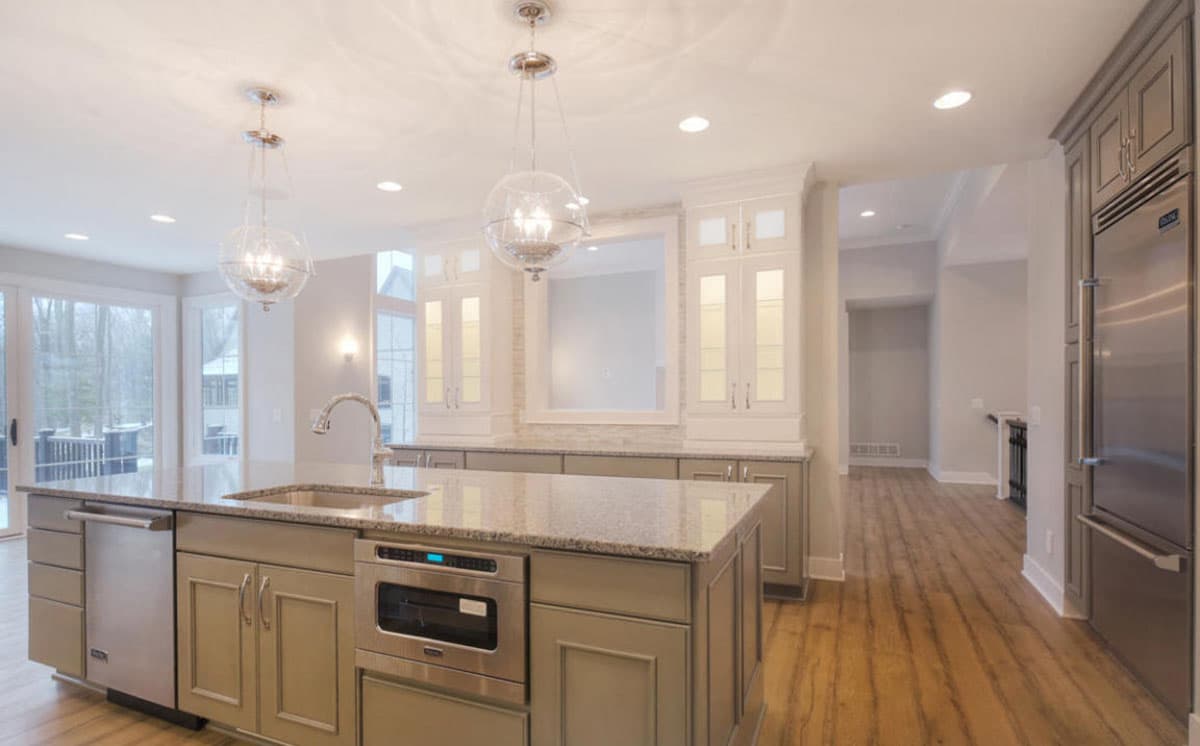 Kitchen interior with island sink, dishwasher, microwave, built-in cabinets, and stainless steel refrigerator.