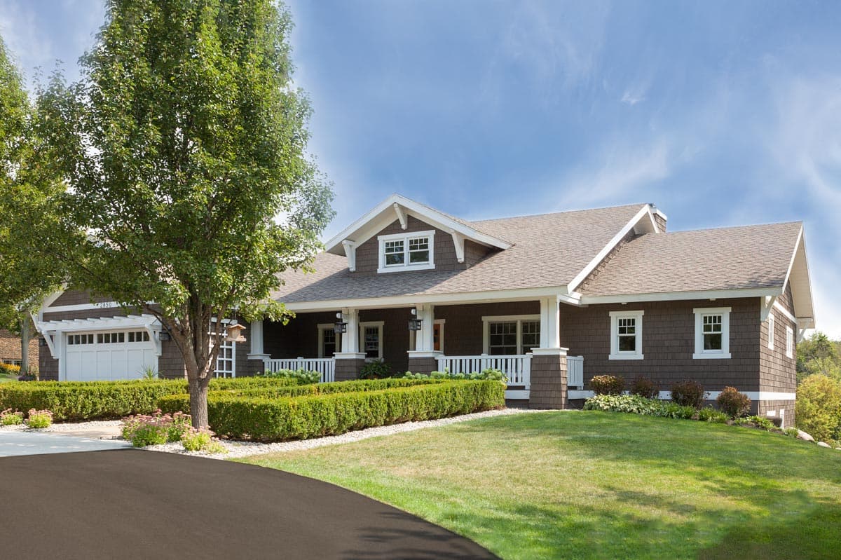 House plan exterior. Craftsman style, one-story. Features a covered front porch with columns, gables, and shake siding. Attached garage on left.