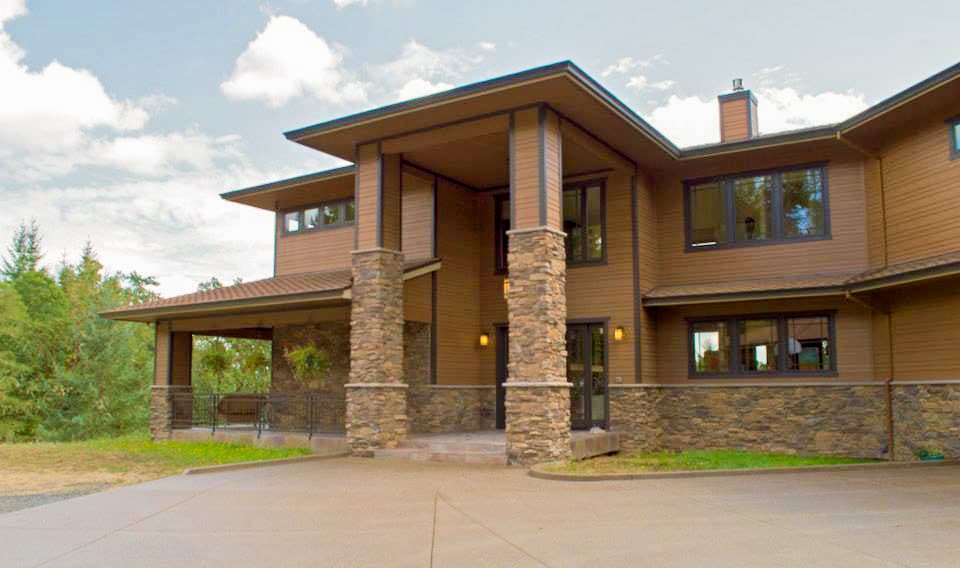 Modern house plan exterior with stone-clad columns, broad eaves, horizontal siding, and a covered porch.