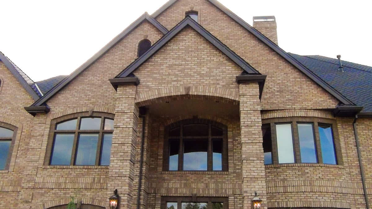 House plan exterior showing a multi-story brick home with multiple gables, arched windows, and a prominent central arched entryway.