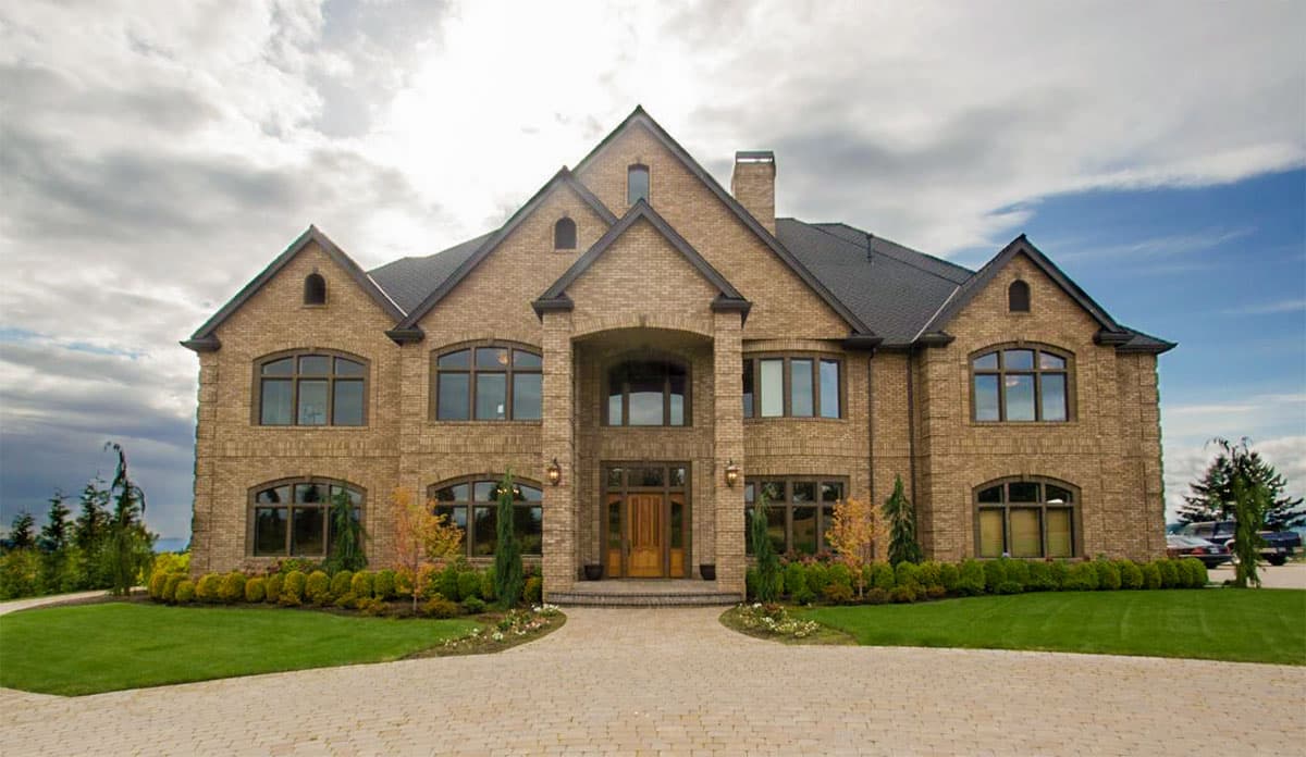Two-story house plan exterior featuring brick facade, arched entry, multiple gables, and a dark roof.  Rounded top windows are used throughout.