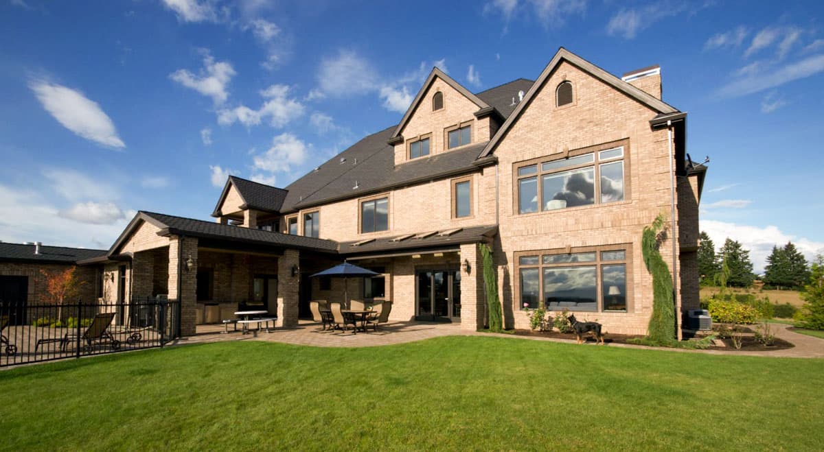 House plan exterior: multi-story brick home with gables, dormers, covered patio, and outdoor kitchen.