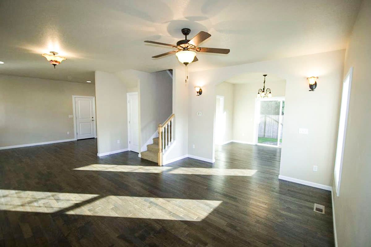 Interior view of a house plan showing an open living area with a staircase, dark wood floors, and arched entryway to dining area.