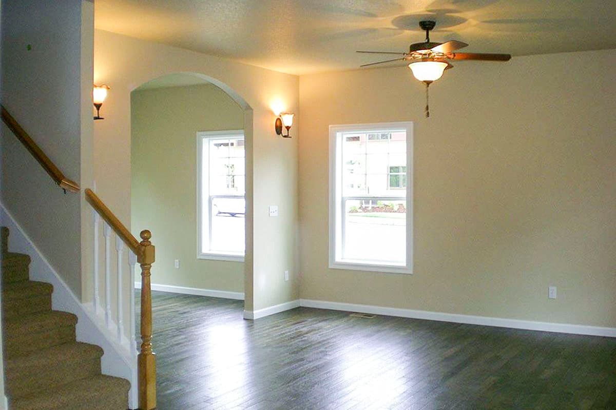 Interior view of a living area with a carpeted staircase, arched doorway, two windows, and wood-look flooring.