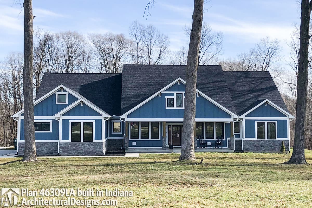 House plan exterior: Blue, one-story Modern Farmhouse with stone base, gables, dormers, and a full-width covered porch.