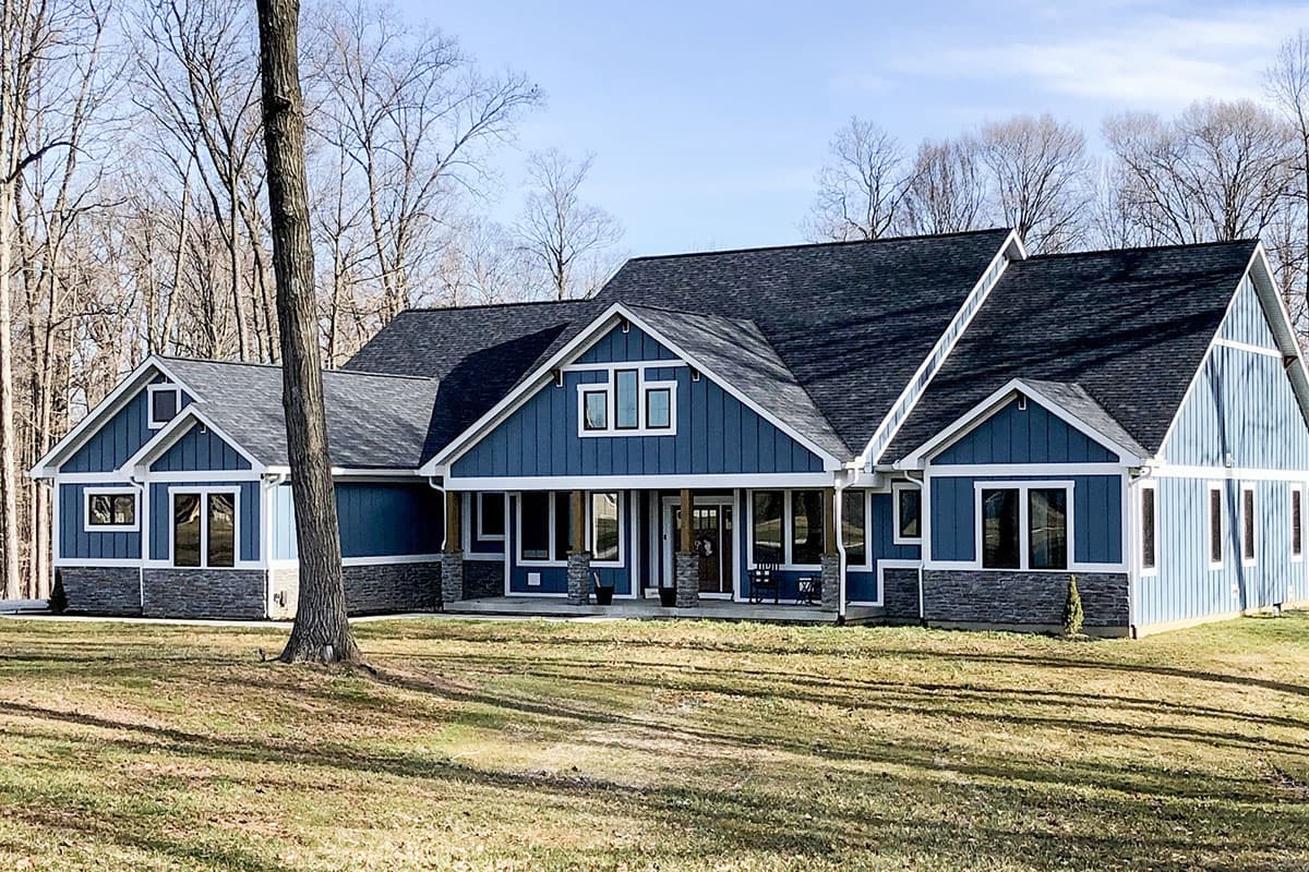 House plan exterior. Craftsman style, single-story home with gables, stone accents, and a covered porch. Features multiple windows and dark roof.