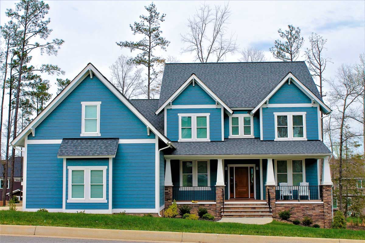 Two-story blue house plan exterior with gables, dormers, and a covered front porch with stone accents.