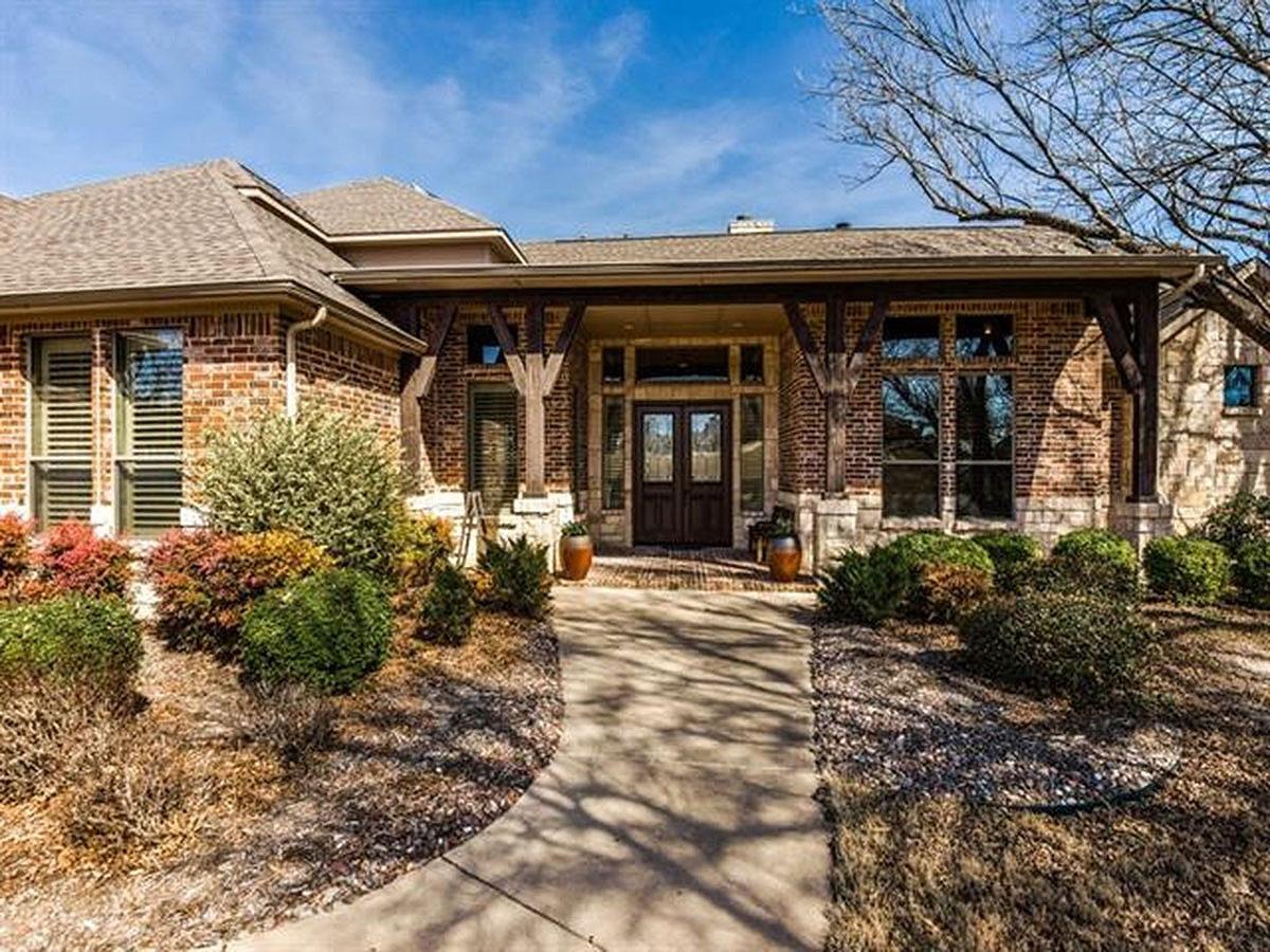 House plan exterior: Brick ranch with prominent timber-framed porch, dual entry doors, and large multi-pane windows.