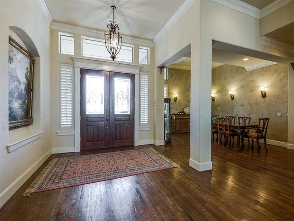Interior view of a house entryway with double doors, arched alcove with art, and view into a dining room with a table set for dinner.