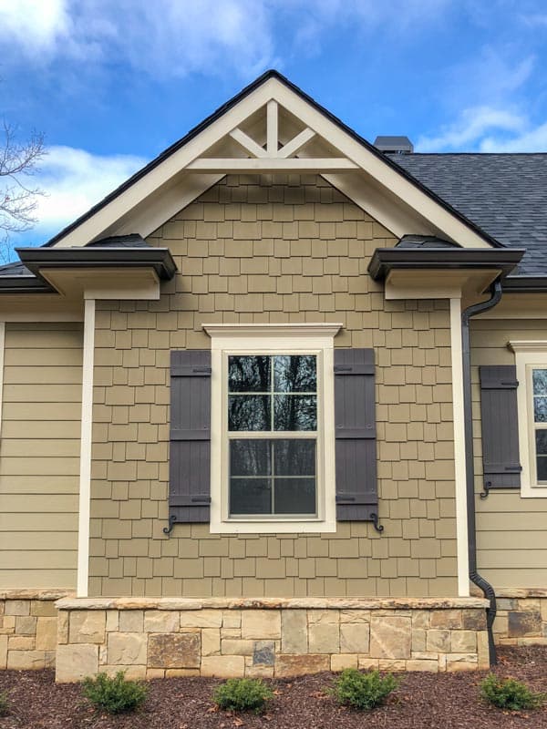 Craftsman house plan exterior with decorative gable truss, shake siding, stone foundation, and dark shutters.